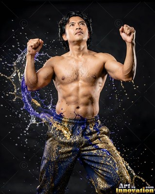Flexing with raised fists, a shirtless man is hit by splashes of blue and gold liquid