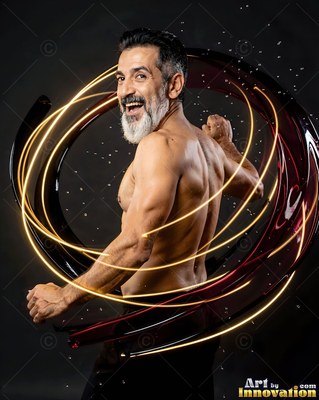 A smiling man with a gray beard turns in a dark studio circled by loops of light