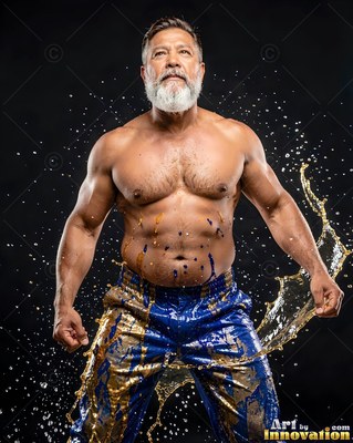 A muscular bearded man flexes his arms as water splashes around his bright blue pants