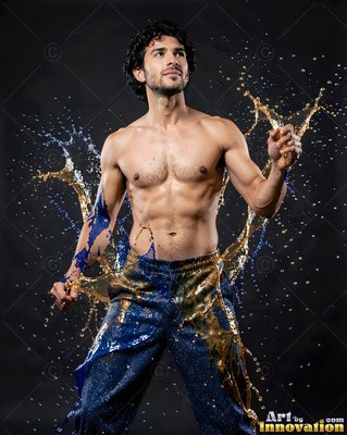 In a dark studio, a shirtless man stands in splashes of blue and gold water