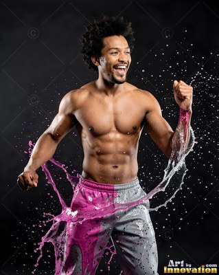 A laughing shirtless man pumps his fists in a dark studio as pink water splashes