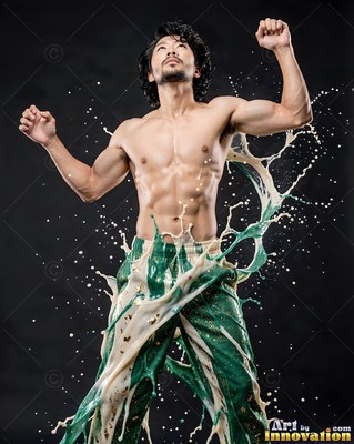 A shirtless man raises his arms as green and white paint splashes off his pants