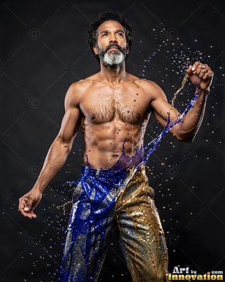 A shirtless man looks up while blue and gold paint splashes across his pants