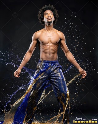 Standing shirtless, a muscular man poses as blue and gold water splashes past his pants