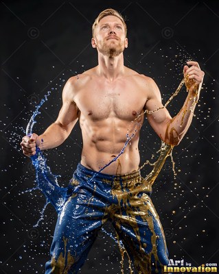 A shirtless man tosses splashes of blue and gold water from his hands