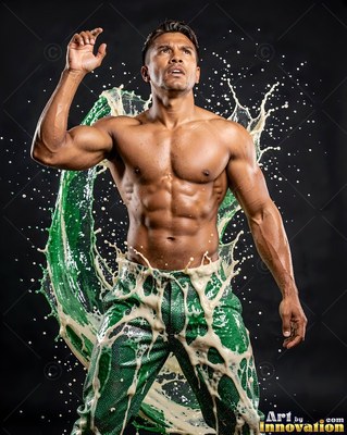 In a dark studio, a shirtless man looks up as green and white liquid splashes around him
