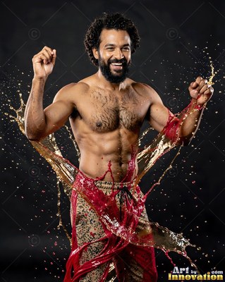 Hairy chest bare, a laughing man in patterned pants gets splashed with red fluid in a studio
