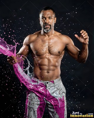 A shirtless muscular man is hit with splashing pink liquid against a dark backdrop