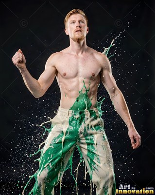 Standing in a dark studio, a shirtless man is splashed with green paint