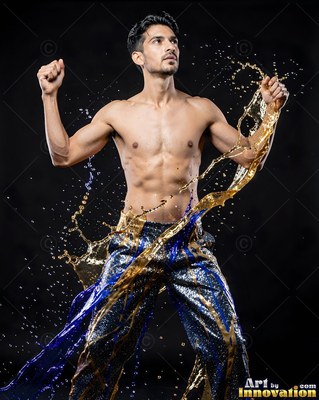 Blue sequined pants on a shirtless man dodging a splash of gold liquid in a dark studio
