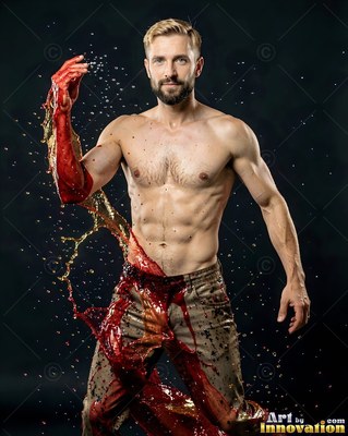 Standing shirtless in a studio, a man caught in red liquid splashing across him