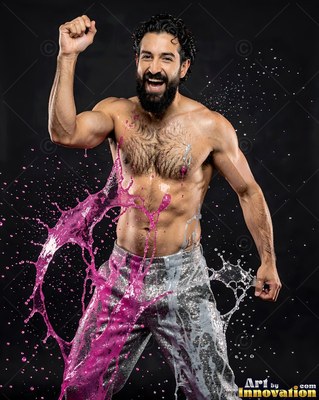 Silver pants on a shirtless, cheering man hit by pink and clear splashes against a dark background