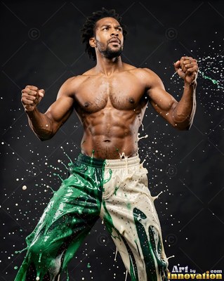 Standing with fists raised in a dark studio, a muscular man splashes green and white paint