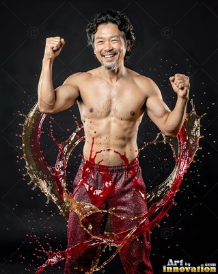 Posing with raised fists, a shirtless man smiles inside an arc of splashing liquid