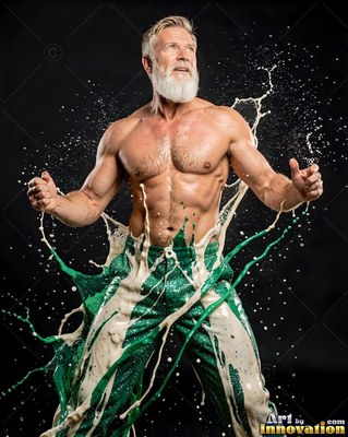Flexing his arms, a shirtless bearded man is splashed with green and white liquid