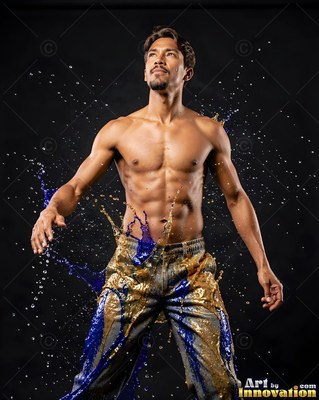 A shirtless man looks up while blue and gold liquid splashes over his pants