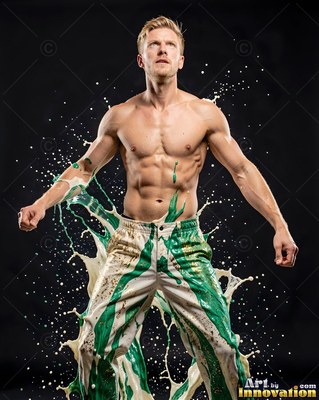 Standing in a studio, a shirtless man has green and cream liquid splashing off his pants