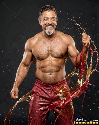 Wearing red trousers, a muscular smiling man poses in a dark studio as red and gold water splashes