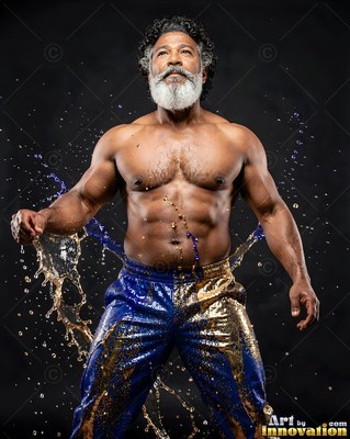 Muscular bearded man standing in a studio as water splashes from his blue pants