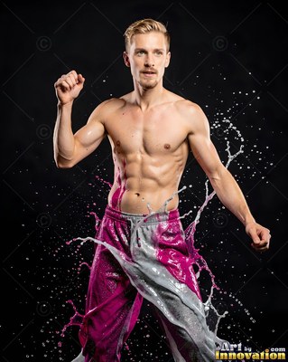 In a dark studio, a shirtless man poses as water splashes around his pants