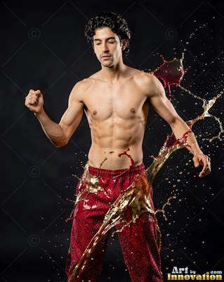 A shirtless man poses as splashes of dark red and amber liquid fly past him