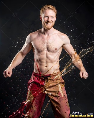 Smiling against a dark studio, a shirtless redheaded man gets hit with red water