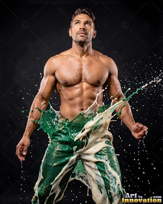 Bare-chested man in green pants splashed with white liquid in a dark studio