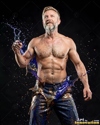 Shirtless man splashed with blue and gold liquid on dark background