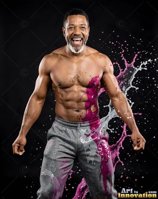 Standing facing forward in a dark studio, a smiling man is splashed with pink fluid