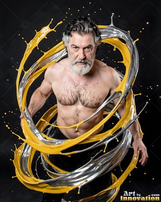In a dark studio, a shirtless man is encircled by swirling yellow and silver paint