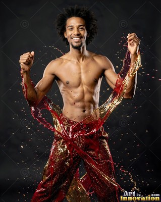 A shirtless man smiles as red and gold water splashes up