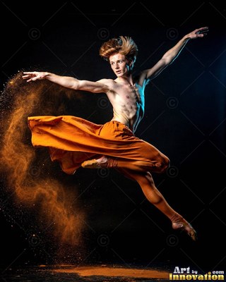 In a dark studio, a shirtless man leaps in orange pants through brown dust
