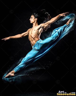 Leaping in midair, a shirtless man in blue pants kicks up blue powder in the dark