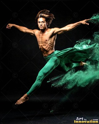 Leaping midair in a dark studio, a shirtless man kicks through green powder dust