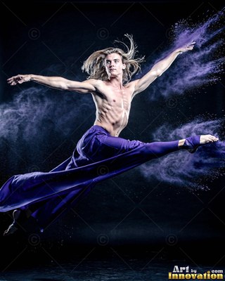 A shirtless man leaps in split legs through a cloud of purple powder
