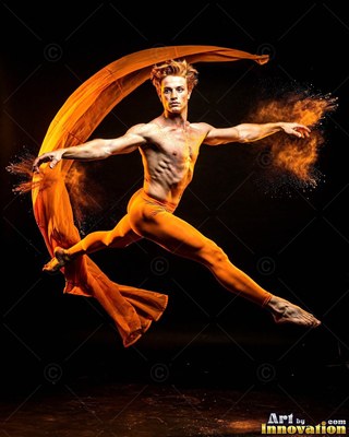 In a dark studio, a man in orange tights leaps with flowing fabric and powder