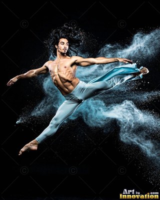 Leaping in midair, a shirtless man splits his legs through a cloud of blue powder