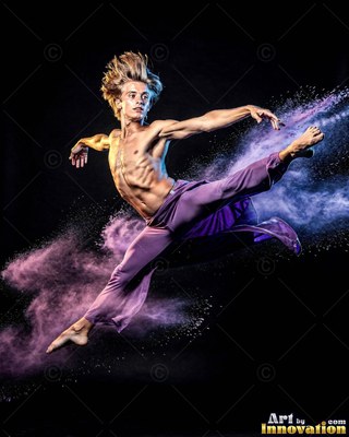 Wearing loose purple pants, a shirtless man leaps through a cloud of purple powder against black