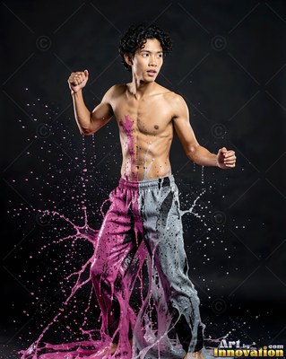 Shirtless man splashed with pink and gray paint against a dark backdrop