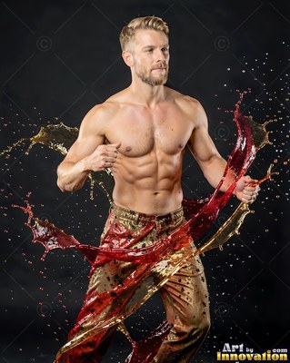 In a dark studio, a shirtless man moves as red and gold water splashes around him