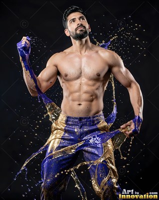 A shirtless man splashed with purple and gold paint on dark background
