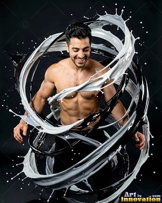A shirtless, smiling man in a dark studio is encircled by spinning rings of black and white paint