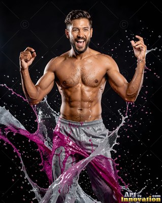Standing in a dark studio, a shirtless man flexes as pink liquid splashes up around him