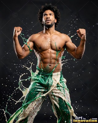 Flexing his arms, a shirtless man is splashed with green and white paint