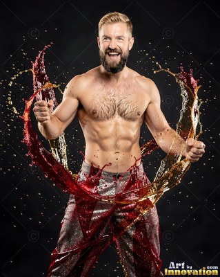 A smiling shirtless man pumps his fists as red and gold liquids splash around him