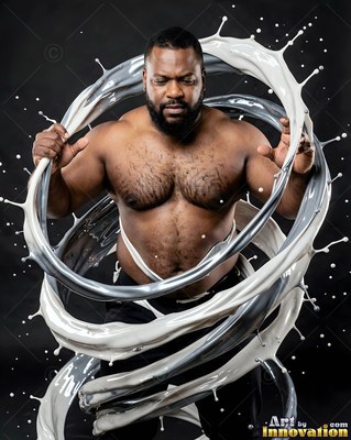 Standing shirtless, a bearded man is encircled by rings of splashing white paint