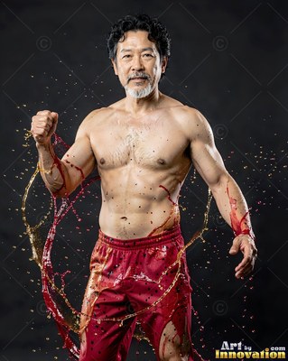 A shirtless man poses as red and gold water splashes around him
