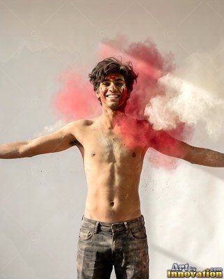 A smiling shirtless man spreads his arms as red and white powder explodes behind him