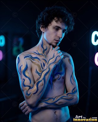 Half-turned in a dark studio, a shirtless man touches his chin under cool blue light