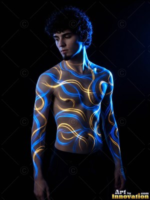 Standing in the dark, a shirtless man has blue and yellow light projected on his skin